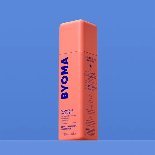 Un flacon de BYOMA Balancing Face Mist, vue en angle montrant les étapes de la routine "Boost Your Barrier" sur le panneau latéral, sur fond bleu.