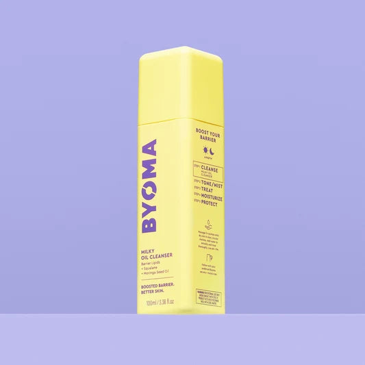Un flacon jaune de Byoma Milky Oil Cleanser, vue en angle montrant les étapes de la routine "Boost Your Barrier" sur le panneau latéral, sur fond violet.