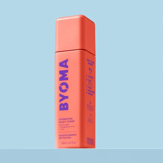 Un flacon de Byoma Hydrating Milky Toner, vue en angle montrant les étapes de la routine "Boost Your Barrier" sur le panneau latéral, sur fond bleu.